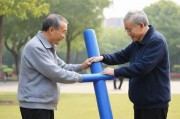 -公园晨练，退休工人张建国在社区公园带领一群老年人进行健身活动，使用自制的大号健身器材锻炼身体，展现老年人积极向上的精神风貌